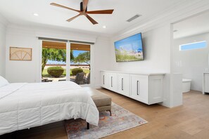 A modern bedroom with a large bed, a ceiling fan, a TV, and a view of the outdoors. - BEAUTIFUL never before seen golf course home in "THE GRAND" (Surprise)