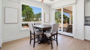 A dining area with a dark wooden table and four chairs, large windows with a view of greenery, and a ceiling fan. - BEAUTIFUL never before seen golf course home in "THE GRAND" (Surprise)