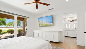 A bedroom with a large bed, a ceiling fan, a TV, and a view of the outdoors. - BEAUTIFUL never before seen golf course home in "THE GRAND" (Surprise)