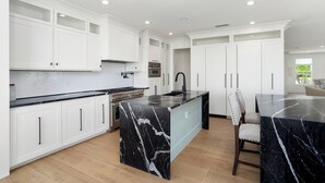 A modern kitchen with white cabinetry, a black marble island, and a built-in oven. - BEAUTIFUL never before seen golf course home in "THE GRAND" (Surprise)