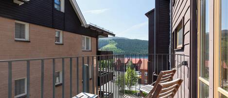 A balcony with wooden chairs and a view of a lake and mountains.