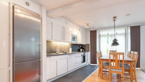 Una cocina moderna con armarios blancos, un refrigerador de acero inoxidable y un comedor con sillas y una mesa de madera.