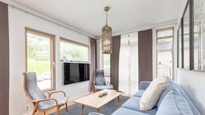 Una sala de estar moderna con un sofá, dos sillones, una mesa de centro y un televisor.