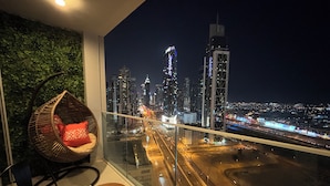 A balcony with a cityscape view at night, a wicker chair, a small table with a bowl, and a green wall. - Downtown Dream Sea View Near Dubai Mall (Dubai)