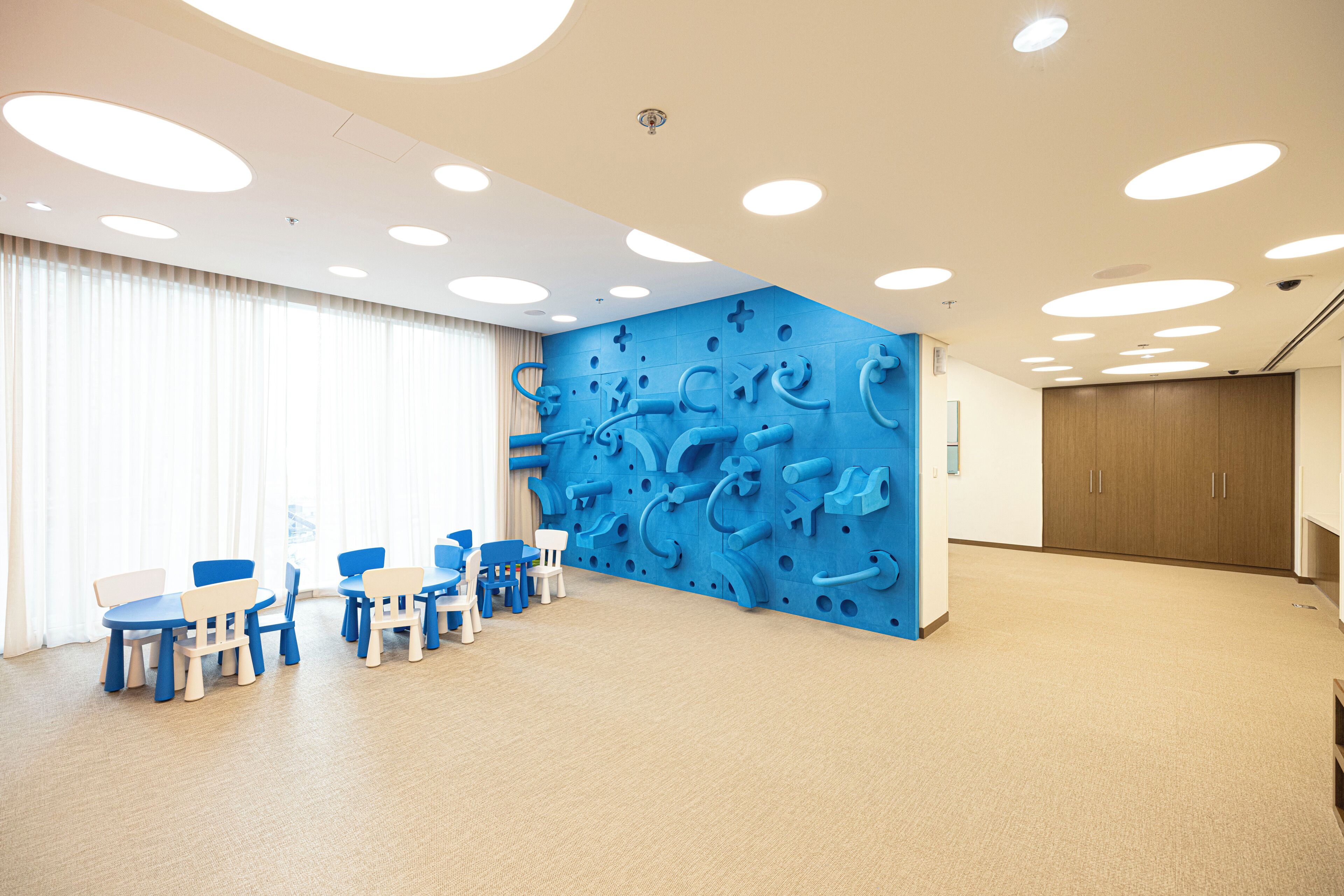 A spacious room with a large window, a blue wall with a play area, and a wooden cabinet.
