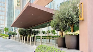A modern building with a glass facade, a covered entrance, and a landscaped area with shrubs and flowers. - Downtown Dream Sea View Near Dubai Mall (Dubai)