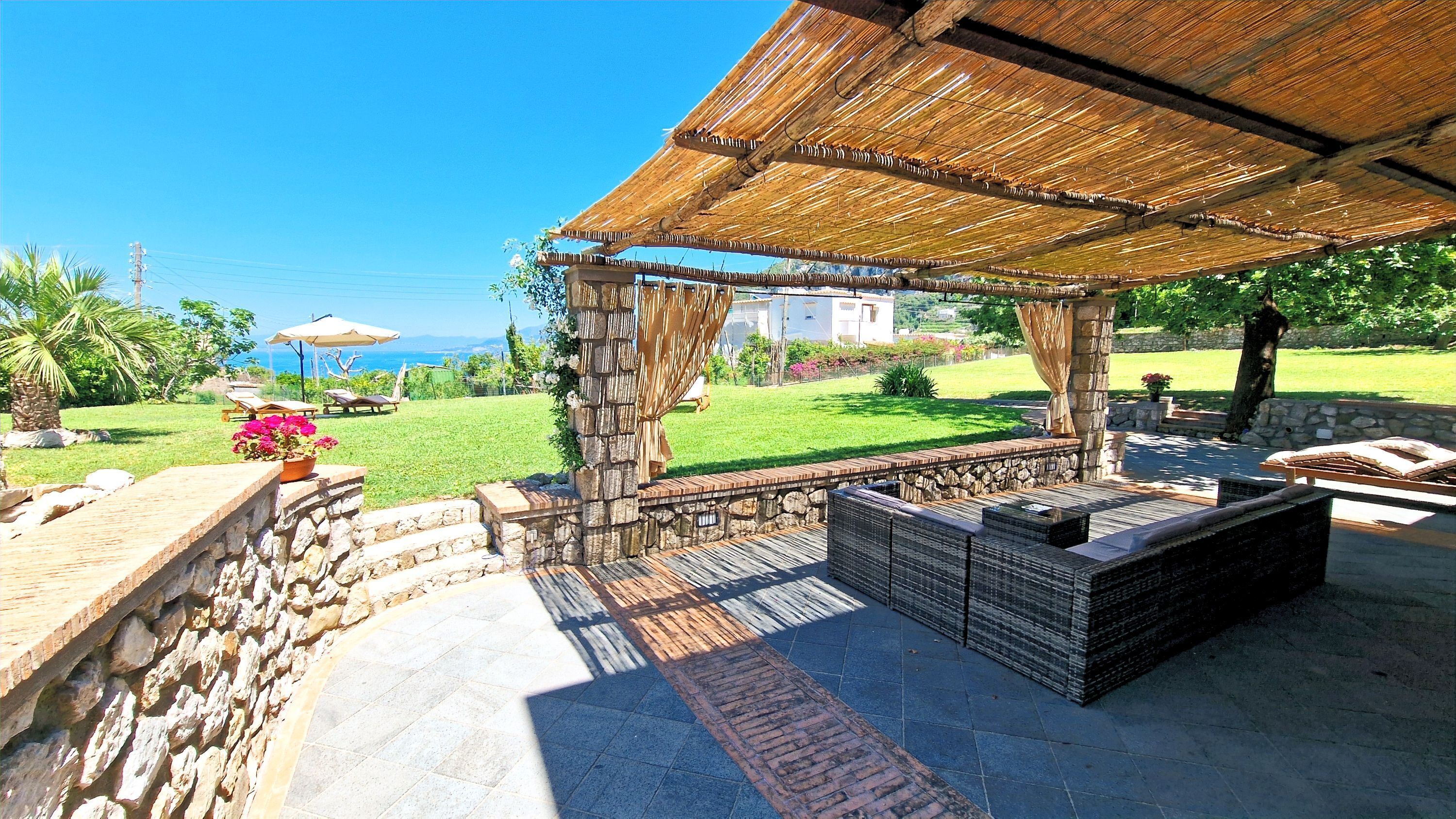A covered outdoor seating area with stone walls and a view of the sea.