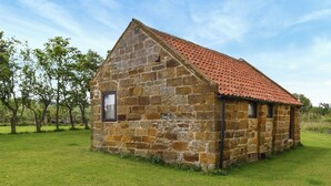 Un edificio de piedra con techo de tejas rojas, rodeado de hierba y árboles.
