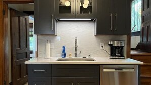 A modern kitchen with dark cabinetry, a stainless steel dishwasher, and a built-in coffee maker. - Historic Elegance in Prime Location! (Milwaukee)