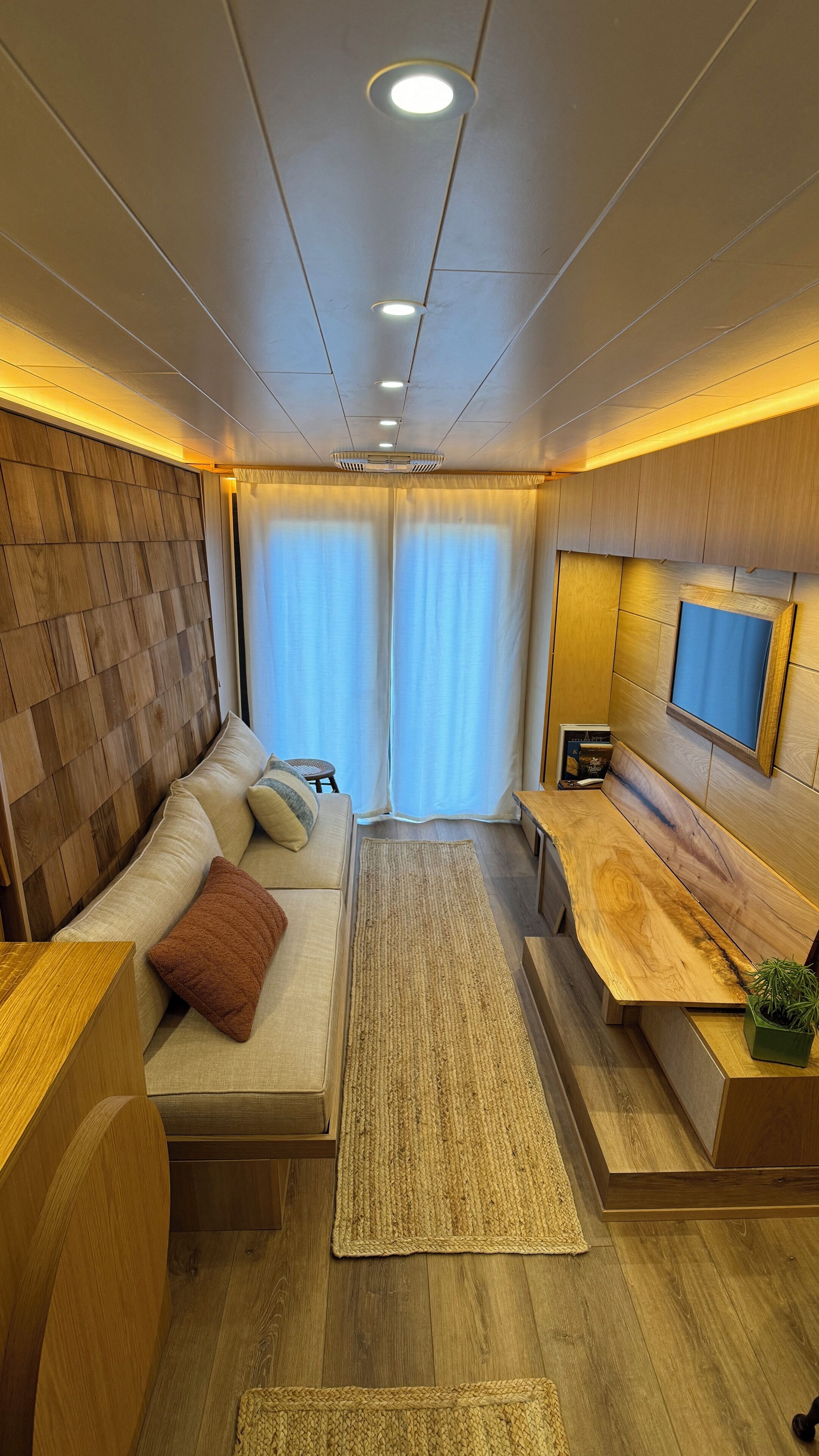 Ein modernes Interieur mit einer Couch, einem kleinen Tisch, einem an der Wand befestigten Fernseher und Holzboden.