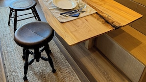 A modern dining area with a wooden table set for two, a small potted plant, and a TV mounted on the wall. - "City Hideaway: Off-Grid Luxe" (Lancaster)
