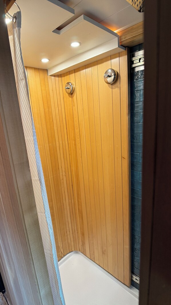 A wooden-paneled shower area with a white floor and a dark tiled wall. - "City Hideaway: Off-Grid Luxe" (Lancaster)