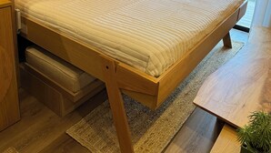 A modern bedroom with a wooden bed, built-in storage, a small bedside table, and a view of the outdoors. - "City Hideaway: Off-Grid Luxe" (Lancaster)