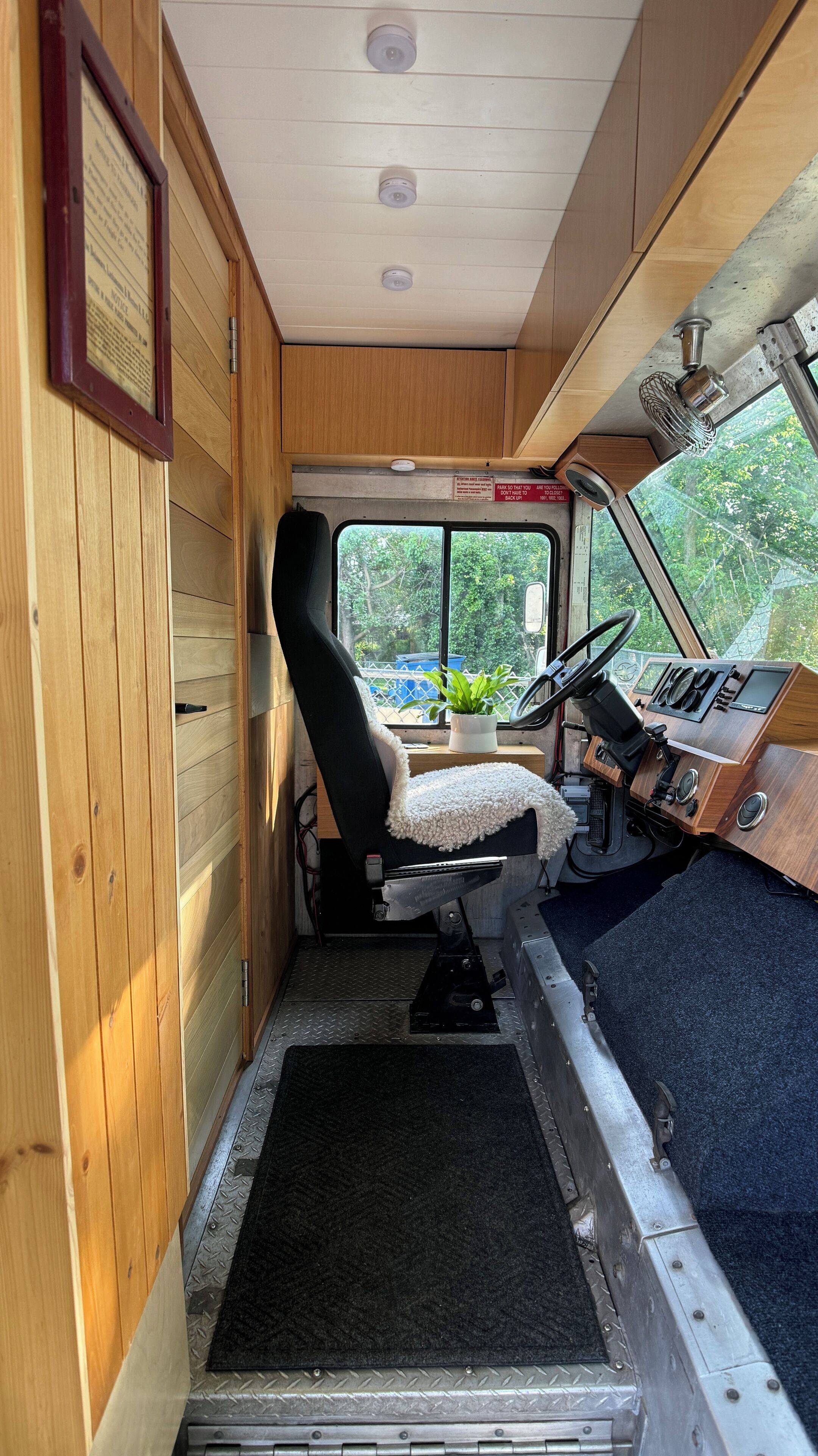 A compact vehicle interior with a wooden panel wall, a steering wheel, dashboard, and a small potted plant.