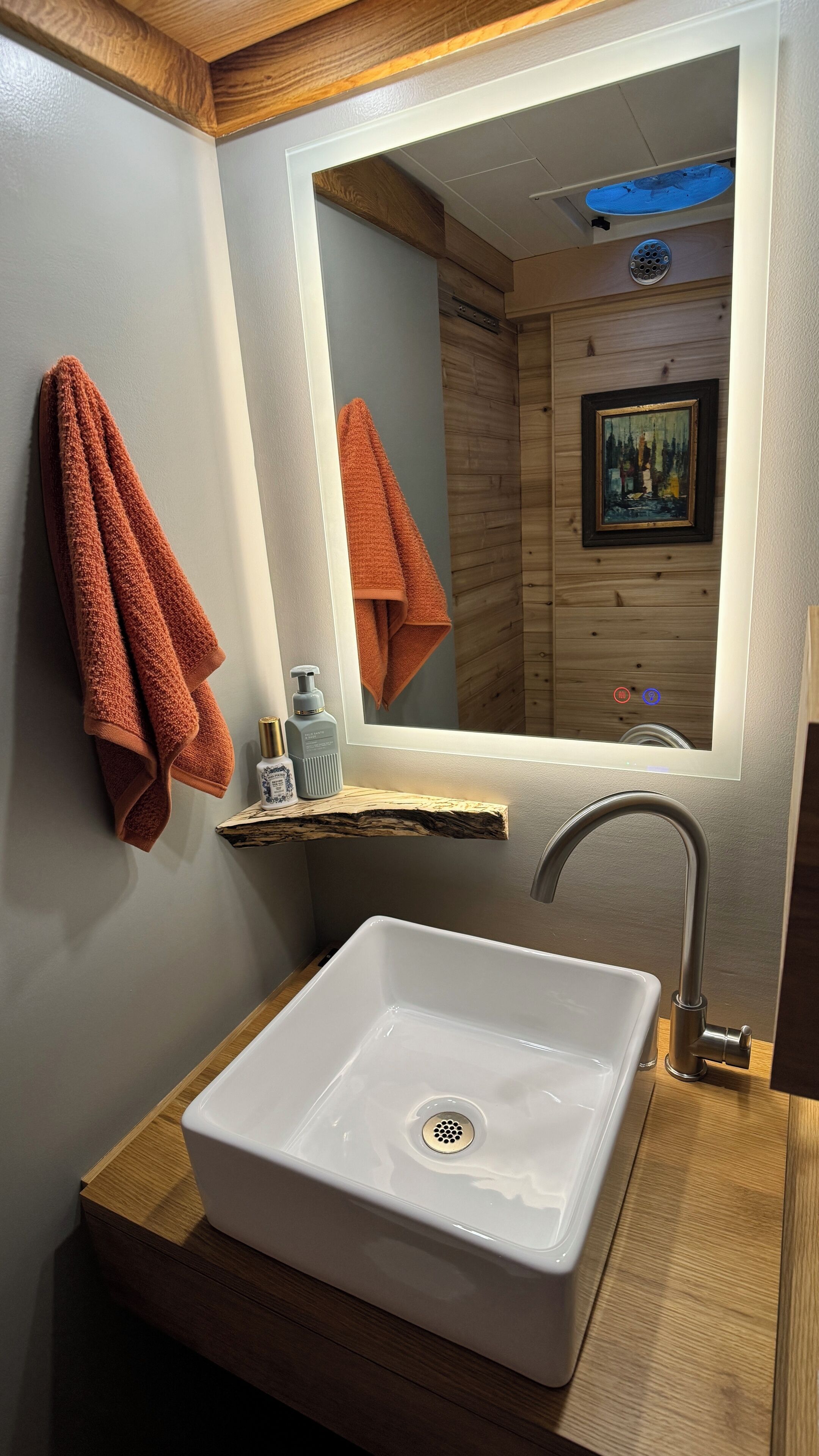 Un bagno con lavandino bianco, mobile contenitore in legno e specchio con luce integrata.