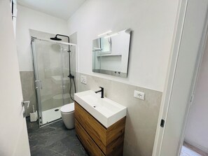 Une salle de bain avec une douche à parois de verre, un lavabo blanc avec un meuble-lavabo en bois, et un miroir au-dessus du lavabo.