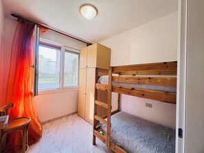 Un lit superposé avec une structure en bois, une chaise, une armoire et une fenêtre avec des rideaux.