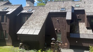 Ein rustikales Blockhaus mit geneigtem Dach, Schornstein und einer kleinen Außenbereich-Sitzgelegenheit mit Tisch und Stühlen.