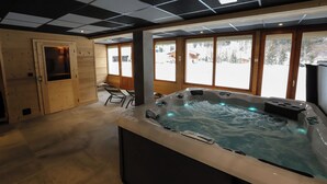 Ein moderner Wellnessraum mit Whirlpool, Holzwänden und großen Fenstern mit Blick auf Schnee.