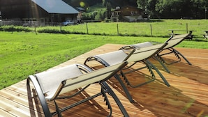 Eine Holzterrasse mit zwei Liegestühlen, die auf eine Wiese mit Bergblick ausgerichtet ist.