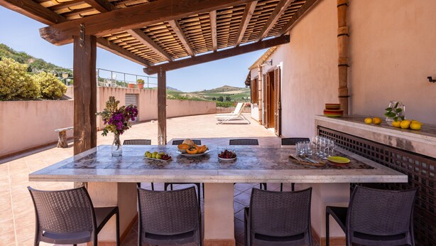 An outdoor patio with a table set for dining, surrounded by chairs, and a pergola overhead. - Villa sui Colli Ericini con Piscina by Wonderful Italy (Erice)