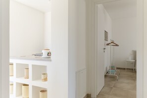 A hallway with a white wall, a coat rack, and a small table with a cup and a book.
