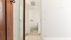 Une chambre d’hôtel avec une porte en bois, un lit, un mur blanc et un couloir menant à une salle de bain équipée d’un porte-serviettes.