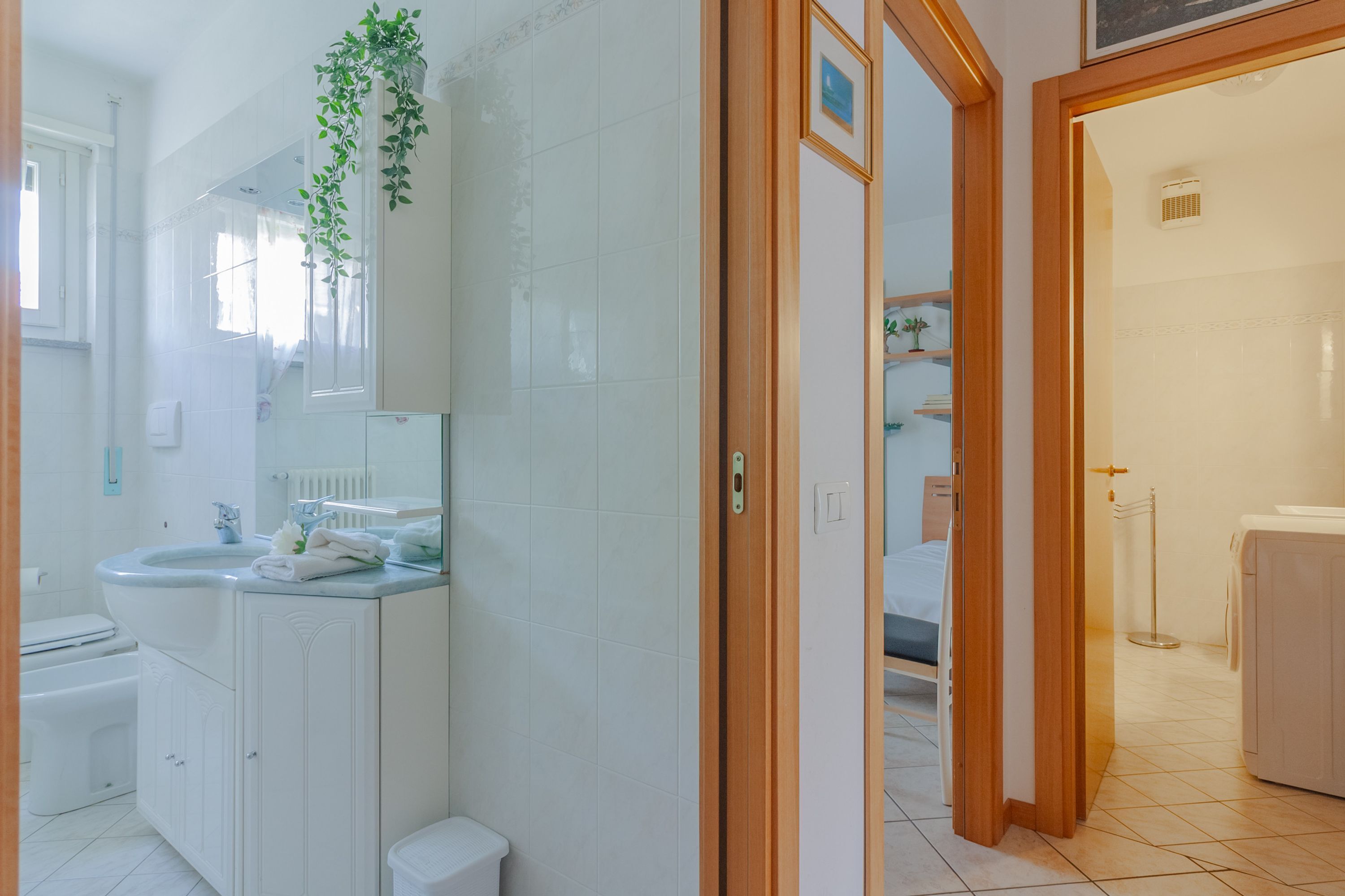 A modern bathroom with a white sink, mirror, and toilet. There is a wooden door leading to another room.