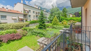 Un edificio residencial con balcones, un jardín con diversas plantas y montañas al fondo.