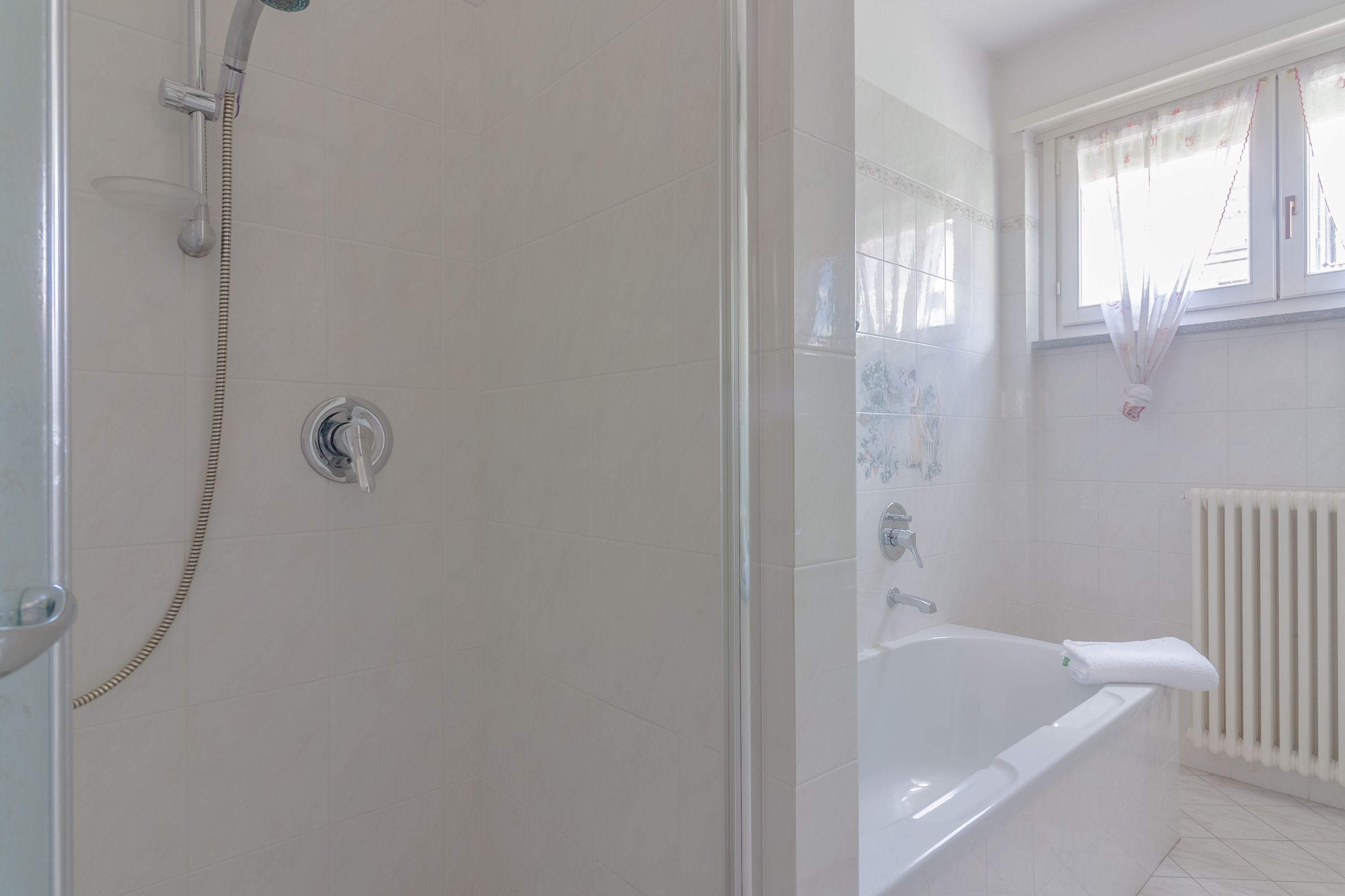 A bathroom with a shower, a bathtub, and a window with curtains.