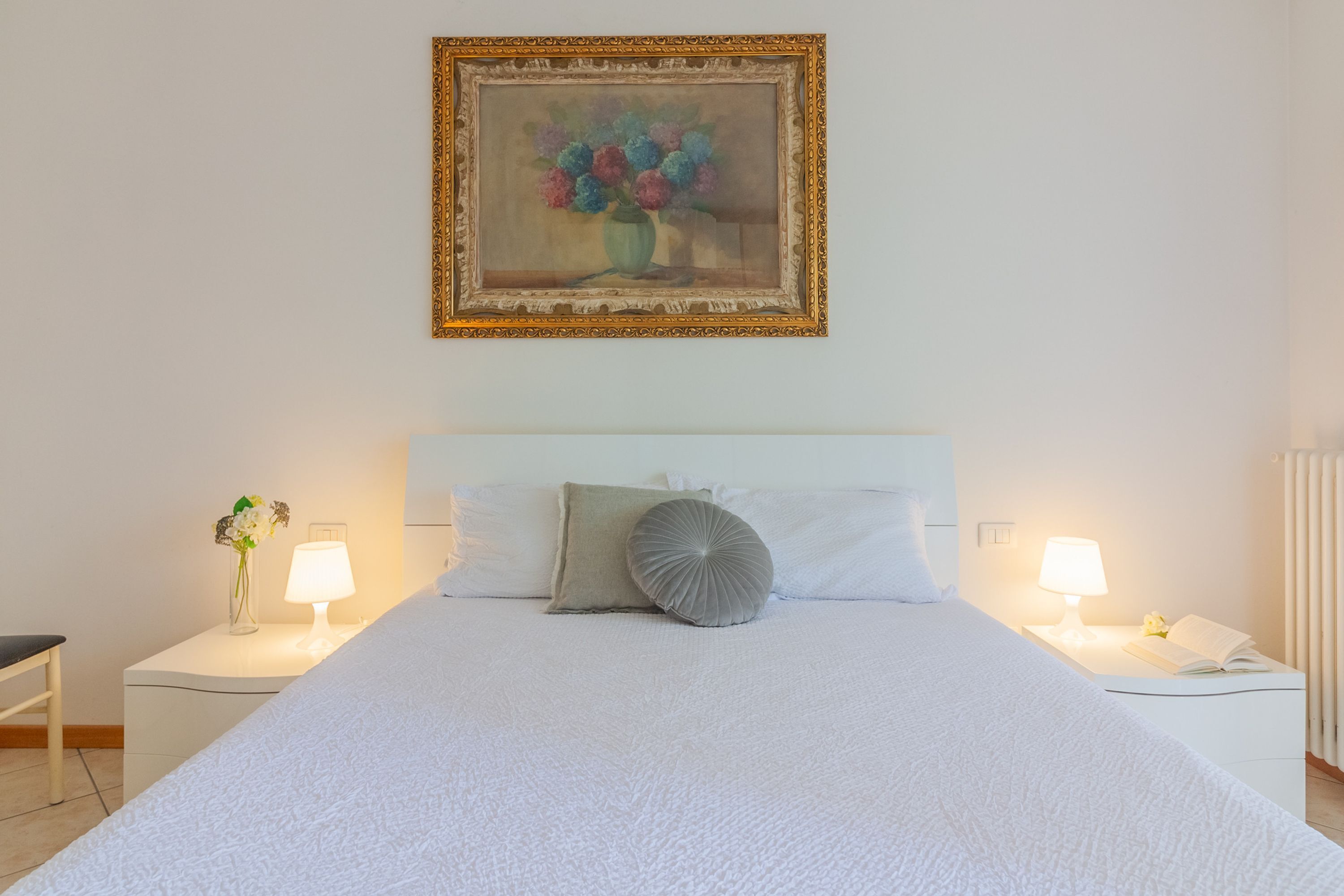A neatly arranged hotel room with a large bed, two bedside tables with lamps, a framed painting above the bed, and a window on the right side.