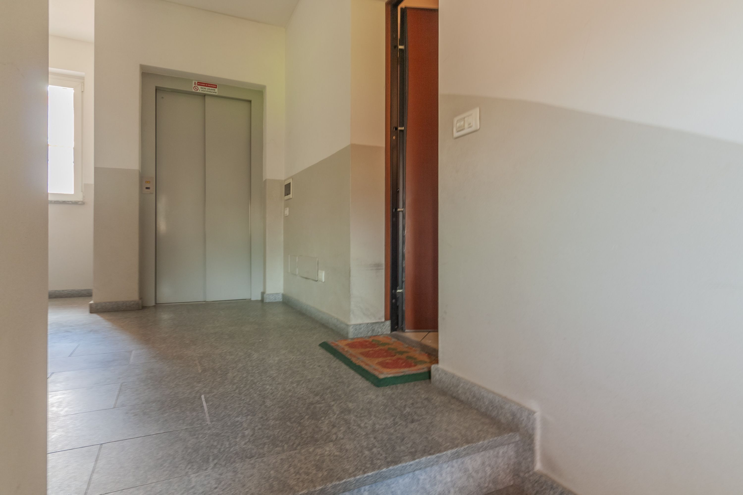 Um corredor com escada coberta por carpete, levando a uma porta com uma placa.