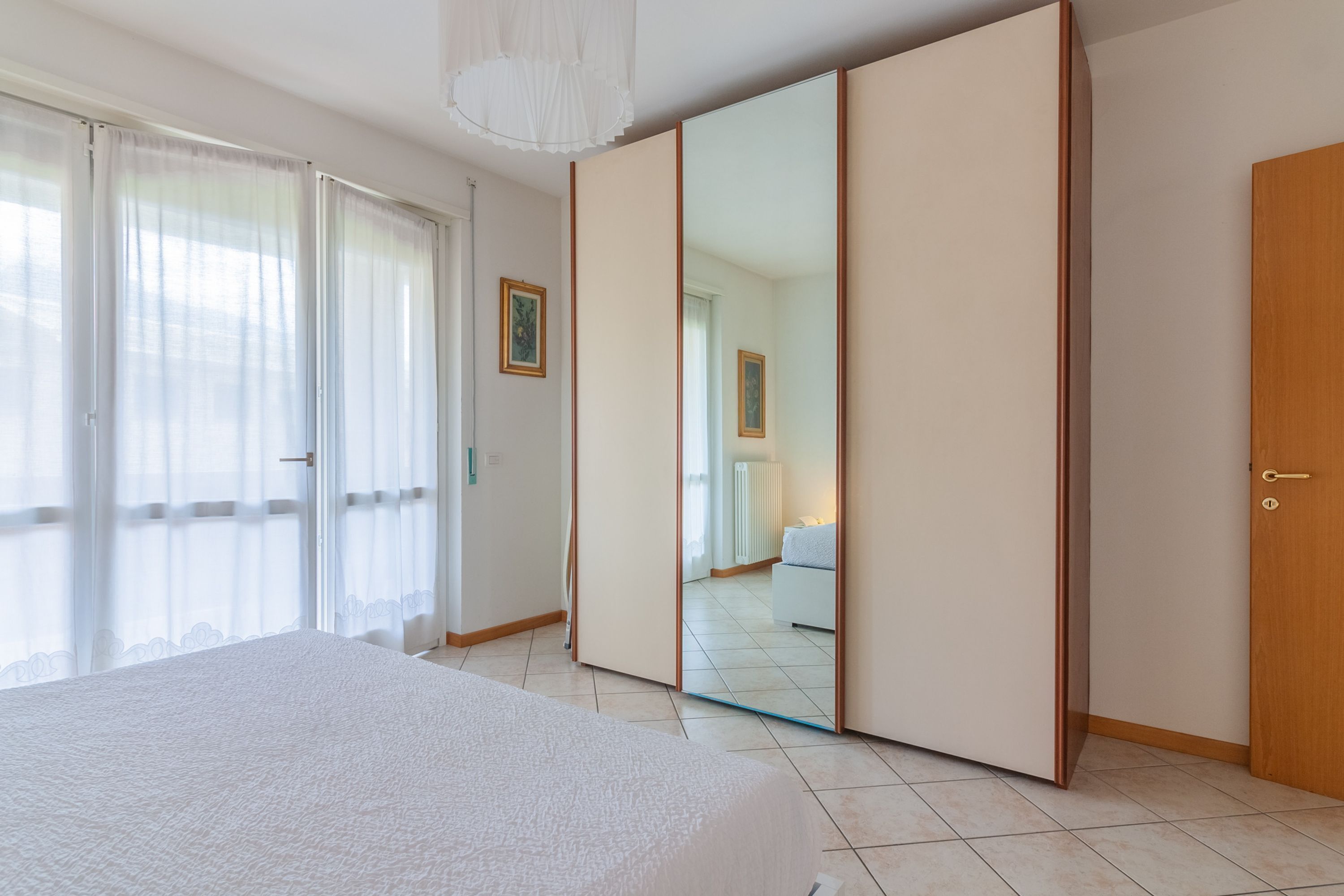 A bedroom with a large bed, a sliding wardrobe, and a mirror reflecting a bathroom.