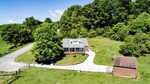 Ein Haus mit grauem Dach, umgeben von üppigen grünen Bäumen und blauem Himmel.