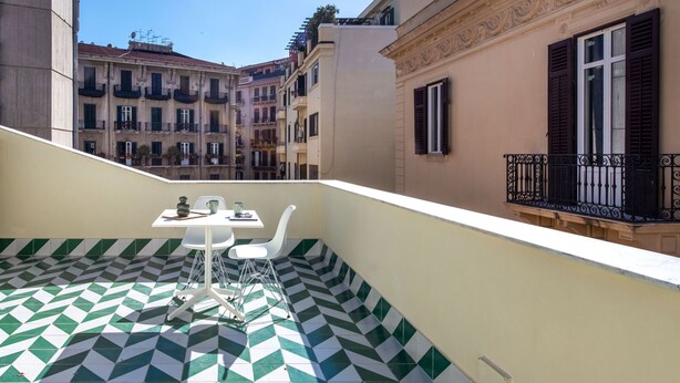 A balcony with a checkered floor, a table with chairs, and a view of adjacent buildings. - Settimo Apartment With Terrace by Wonderful Italy (Palermo)