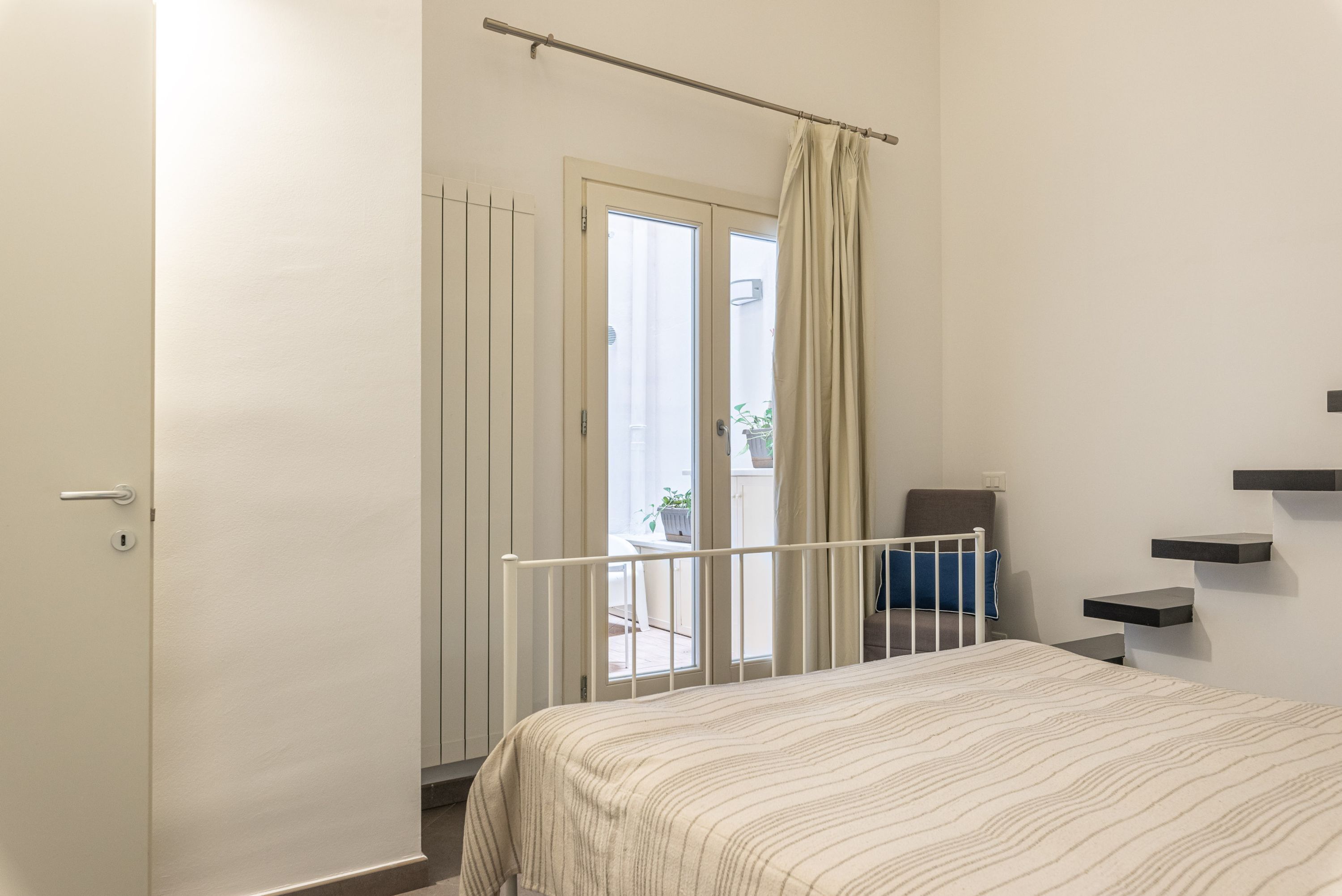 A bedroom with a bed, a door, a curtain, a chair, and a small table.