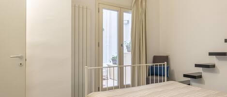 A bedroom with a bed, a door, a curtain, a chair, and a small table.
