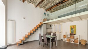 A modern interior with a staircase leading to a loft, a dining area with a glass table, and a kitchen with white cabinets. - Metam Apartment in the City Center by Wonderful Italy (Palermo)