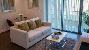 A modern living room with a white sofa, striped pillows, a glass coffee table, and artwork on the walls. - Deluxe 1 Bedroom Apartment in City Road (London)