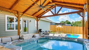 A covered outdoor swimming pool with hot tubs, a barbecue area, and a wooden deck.