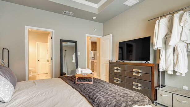 Une chambre à coucher comprenant un lit, une commode, un téléviseur et un dressing avec des vêtements suspendus.