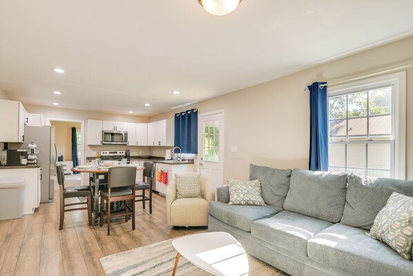 A modern living room with a grey sofa, a dining table, and a kitchen in the background. - Charming Greenville Home w/ Yard: 3 Mi to Downtown (Greenville)