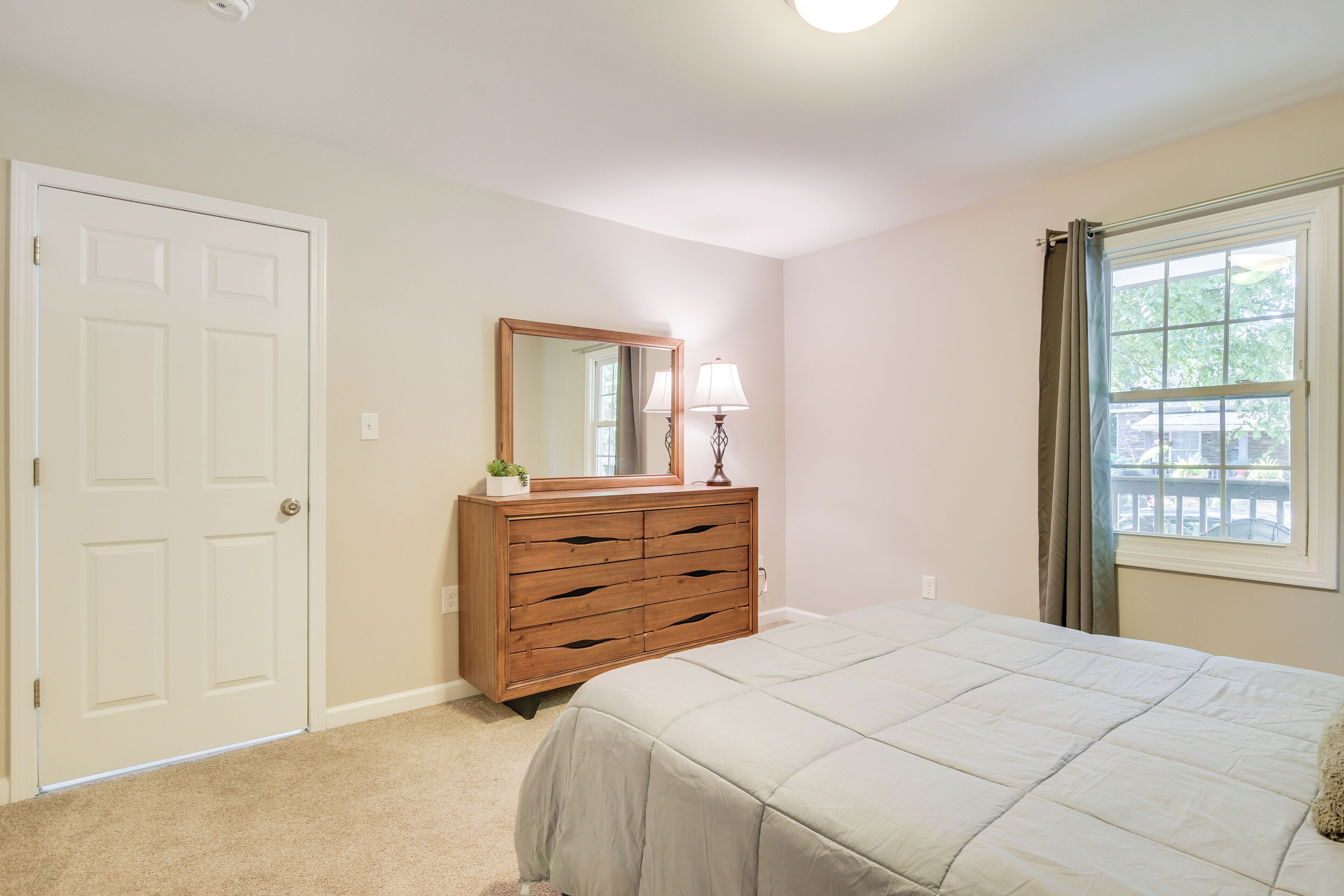 A bedroom with a bed, a dresser, a mirror, and a window with curtains.