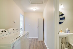A laundry room with a washer and dryer, a door leading to a hallway, and a bathroom with a sink and toilet. - Charming Greenville Home w/ Yard: 3 Mi to Downtown (Greenville)