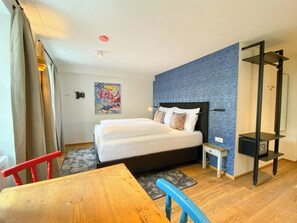 A hotel room with a bed, a small bedside table, a chair, a wooden table, a blue patterned wall, and a red ceiling light. - Blackhome Vintage Innsbruck (Innsbruck)