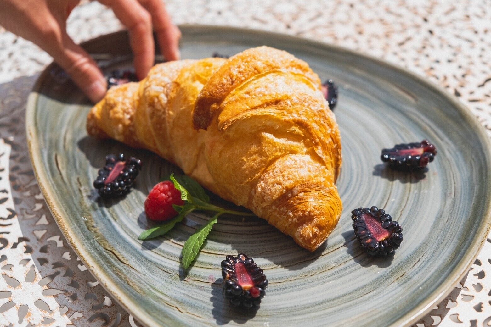 Un croissant sobre un plato de cerámica con zarzamoras y frambuesas.