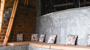A curved bench with cushions against a stone wall, a bamboo ladder, and a rustic ceiling. - Nuwans Countryside Hideaway (Tangalle)