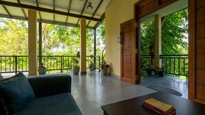 A covered outdoor seating area with a sofa and a table, surrounded by potted plants and a view of lush greenery. - Nuwans Countryside Hideaway (Tangalle)