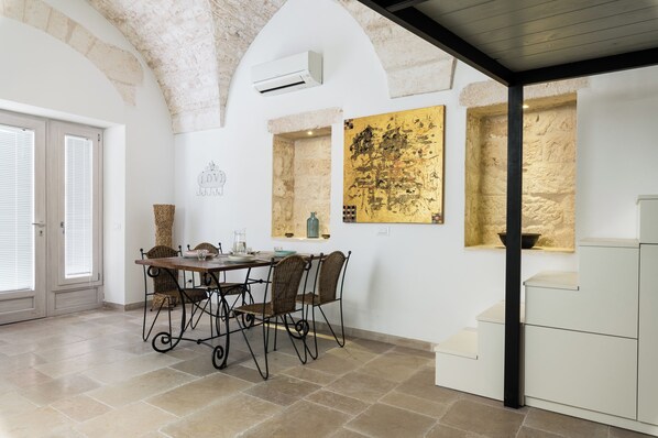 A dining area with a table and chairs, a stone wall, and a window with a view. - Casa Sottosopra by Wonderful Italy Srl (Ostuni)