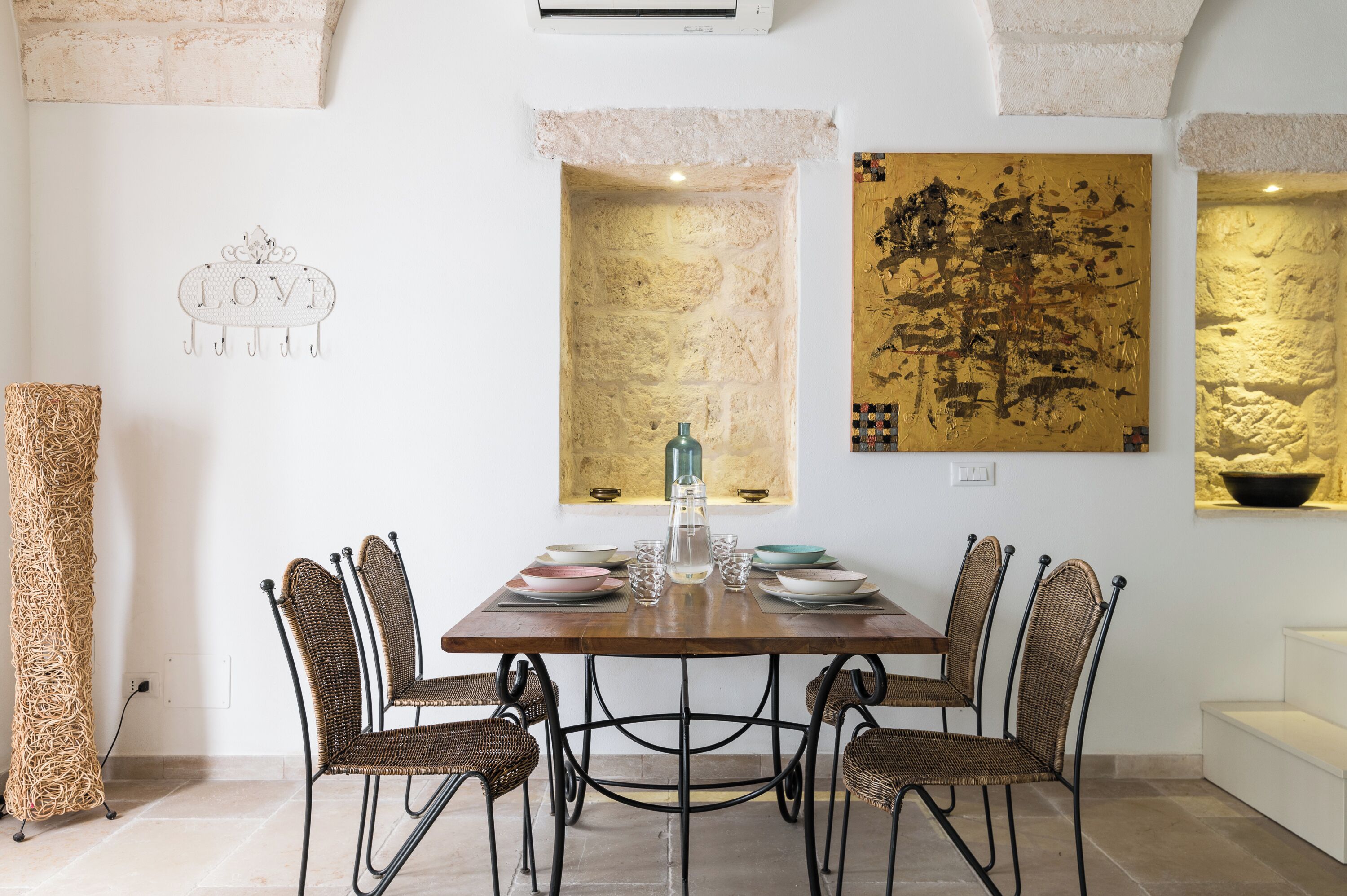 A dining area with a wooden table, wicker chairs, and a decorative wall with a 'LOVE' sign and artwork.